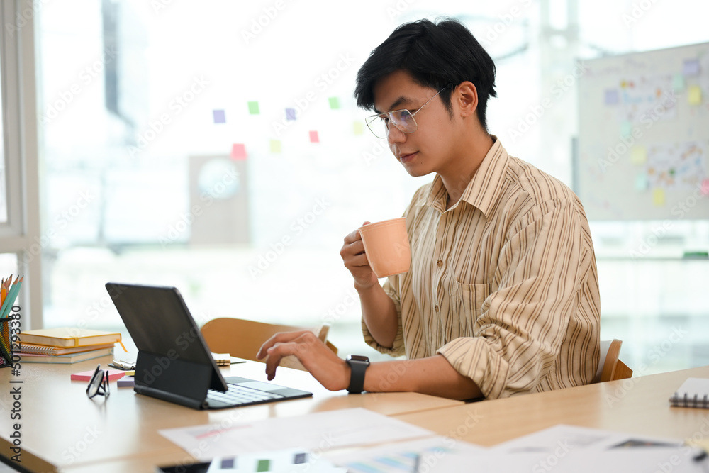 Handsome Asian businessman focused on his work, reading the data on tablet Handsome Asian businessman focused on his work, reading the data on tablet
