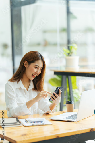 Asian woman in casual clothes is happy and cheerful while communicating with her smartphone and working in a coffee shop.