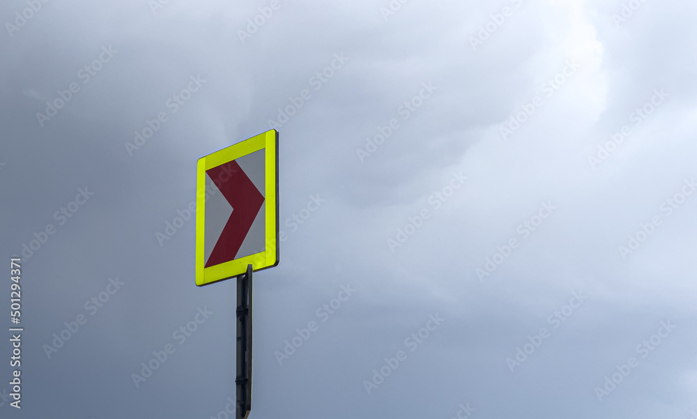 Traffic sign indicator pointing to the direction of the curve on the road against a cloudy sky. Infrastructure industry. Traffic sign indicator pointing to the direction of the curve on the road against a cloudy sky. Infrastructure industry.