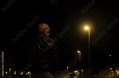Rear view of adult man walking on street at night with lights of street lamps