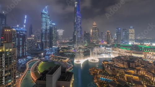 Skyscrapers rising above Dubai downtown all night timelapse surrounded by modern buildings aerial top view