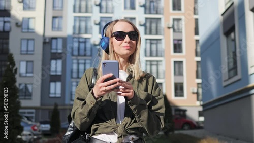 Attractive Female Tourist Walking in City District Listening to Music and Typing Message to friends. Having Free Time on the Summer Weekend. Woman Browsing Internet App. Relaxed. Good Mood. Satisfied. photo