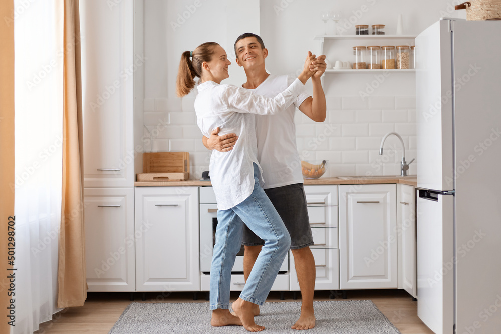 Full length portrait of man and attractive young adult woman dancing kitchen, romantic couple spending time together at home, expressing love and gentle. Full length portrait of man and attractive young adult woman dancing kitchen, romantic couple spending time together at home, expressing love and gentle.