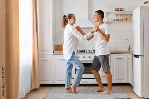 Attractive man and beautiful young woman having fun together in the kitchen, romantic couple is dancing and expressing love, being happy to spend weekend together.