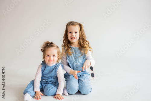 Joyful two little preschool girls have fun playing together in a cozy studio on a white background. Smiling little sisters kids jumping, playing on the weekend. Family concept.