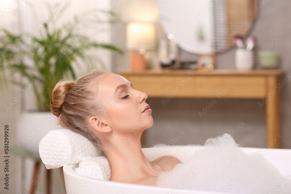 Young woman using pillow while enjoying bubble bath indoors Young woman using pillow while enjoying bubble bath indoors