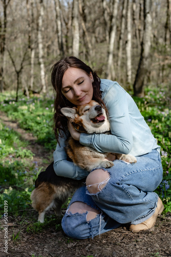 a cute young girl gently hugs a corgi dog in the spring forest