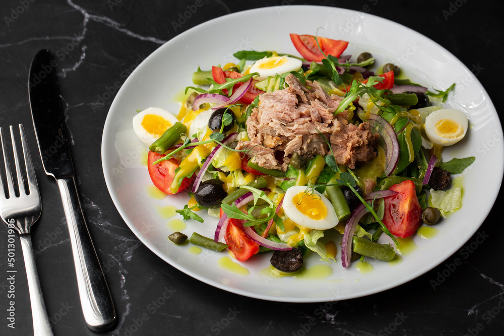 French salad Nicoise with tuna, egg, green beans, tomatoes, olives, lettuce, onions and anchovies on a gray background. Healthy food