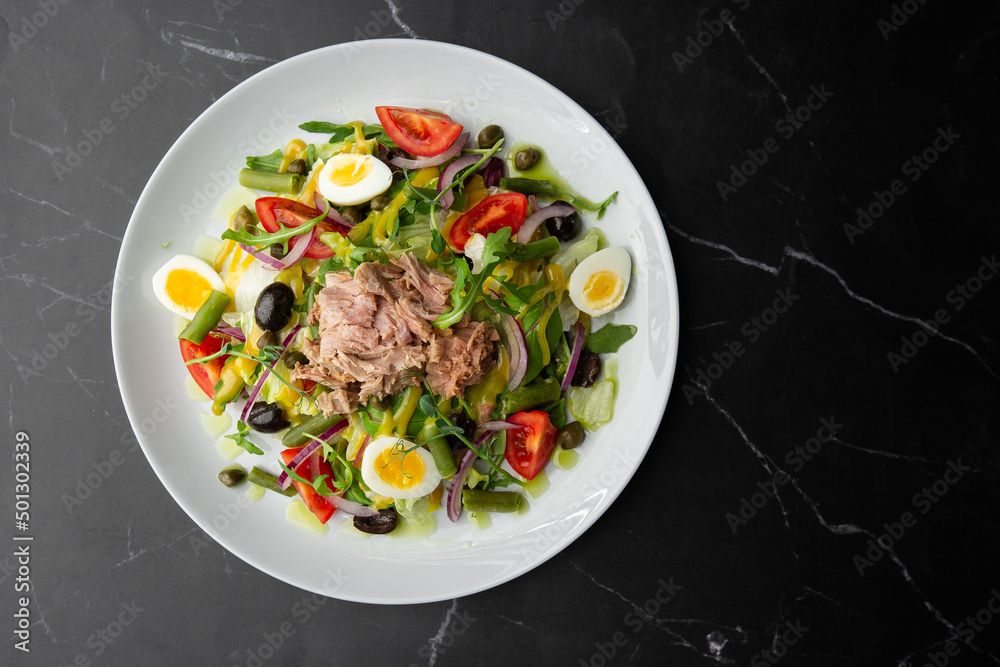 French salad Nicoise with tuna, egg, green beans, tomatoes, olives, lettuce, onions and anchovies on a gray background. Healthy food