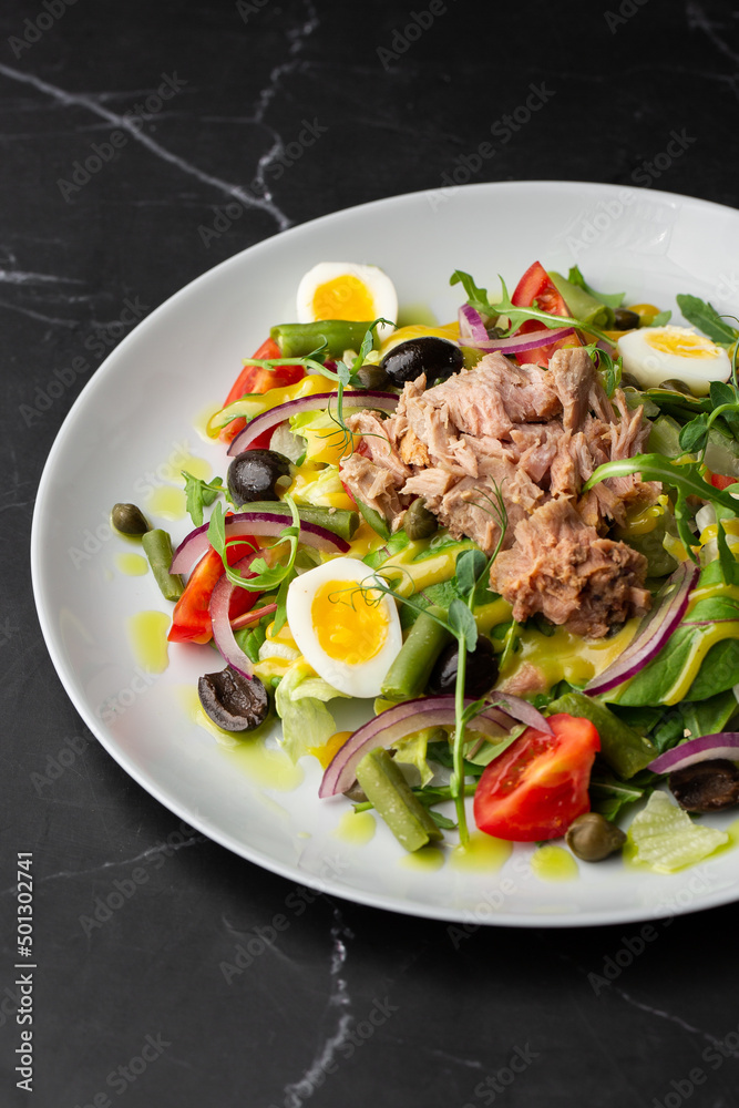 French salad Nicoise with tuna, egg, green beans, tomatoes, olives, lettuce, onions and anchovies on a gray background. Healthy food French salad Nicoise with tuna, egg, green beans, tomatoes, olives, lettuce, onions and anchovies on a gray background. Healthy food