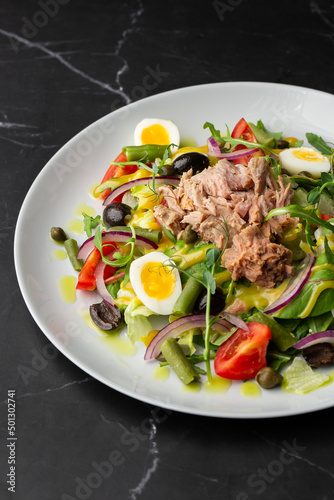 French salad Nicoise with tuna, egg, green beans, tomatoes, olives, lettuce, onions and anchovies on a gray background. Healthy food