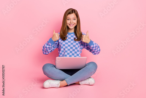 Full length photo of brown hairdo little girl hold laptop thumb up wear sweater jeans sneakers isolated on pink background