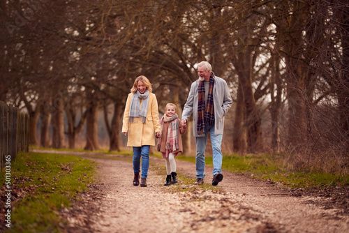 Grandparents With Granddaughter Outside Walking Through Winter Countryside Holding Hands