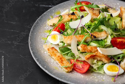 A Caesar salad with grilled chicken breasts, lettuce, croutons, eggs, cherry tomatoes, dressed with Parmesan cheese and sauce.