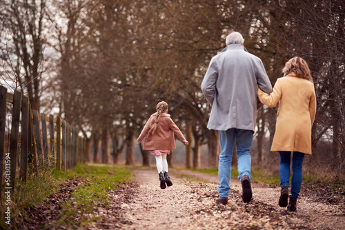 Rear View Of Grandparents With Granddaughter Outside Walking Through Winter Countryside