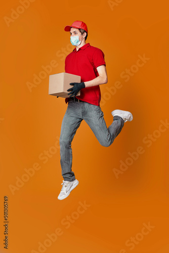 Delivery man in face mask holding cardboard box and jumping