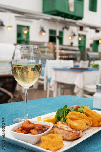 Delicious grilled seafood on plate, dish and glass of white wine in restaurant outdoors.Vertical photo photo