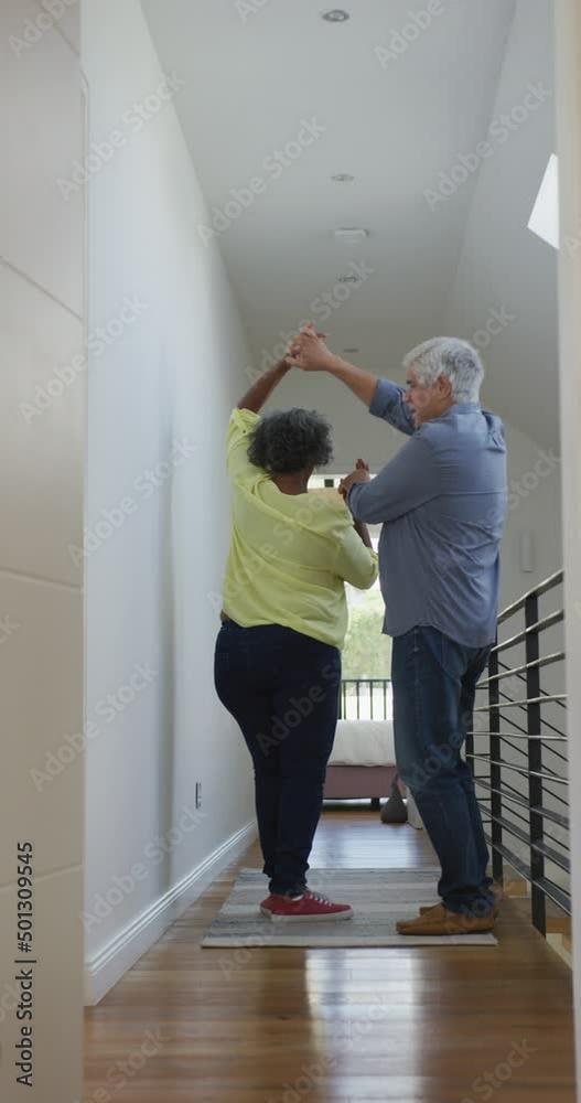 Vertical video of happy diverse senior couple dancing at home