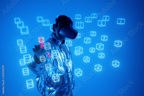 Woman wearing virtual reality simulator touching hologram cube on screen against blue background