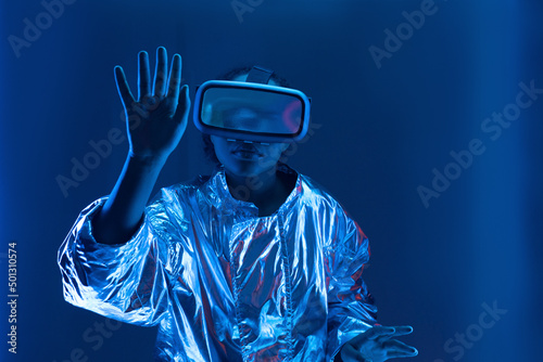 Young woman in virtual reality simulator gesturing against blue background photo