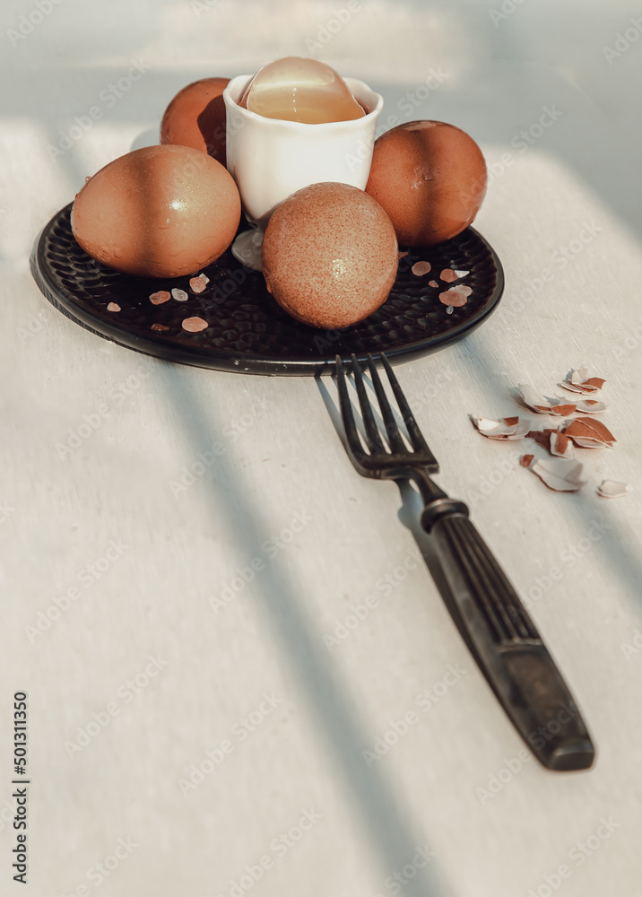 Fototapeta premium Composition of Broken fresh chicken egg (Hen egg) put at the middle of the fresh eggs with brown eggshell and Black antique silver fork on white table. Natural organic healthy food concept, Copy space