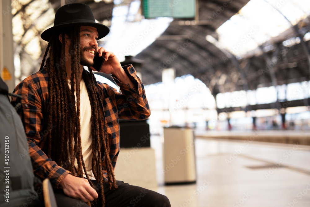 Fototapeta premium Handsome guy at railway station waiting for the train. Young man waiting to board a train. Urban guy using the phone..