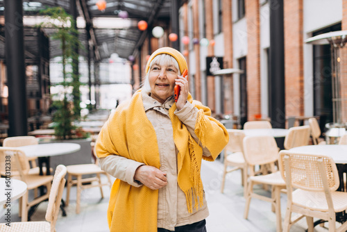 Beautiful smiling female in yellow hat talking on Phone and standing outdoors. Phone Communication. Happy cheerful senior woman walking on city street, Urban lifestyle concept. Traveler
