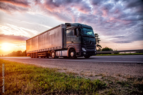 A beautiful truck tractor with a semitrailer transports cargo against the backdrop of a sunset in the evening and a beautiful sky with clouds in summer. Cargo insurance, sanctions