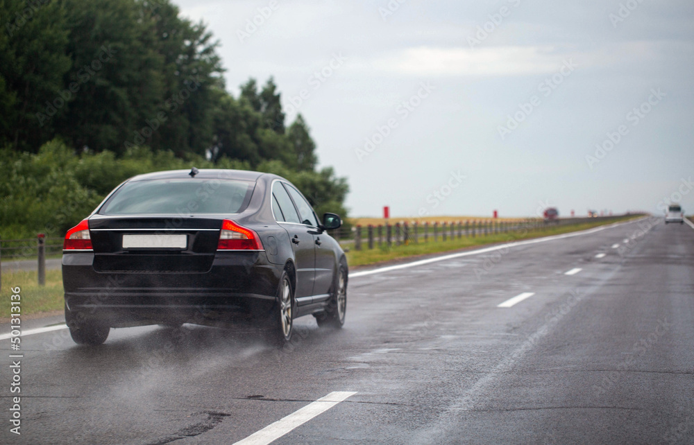 A black passenger car drives on a wet highway in summer. Slippery road. Copy space for text