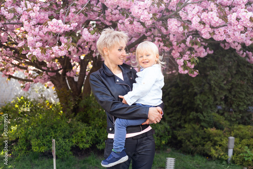 Mother and little son are having fun in the blooming Sakura gardens. Portrait woman hugging little baby boy