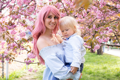 portrait of beautiful mother holds in her arms a little cute son. Mom and little baby boy in a flowering garden. Sakura.
