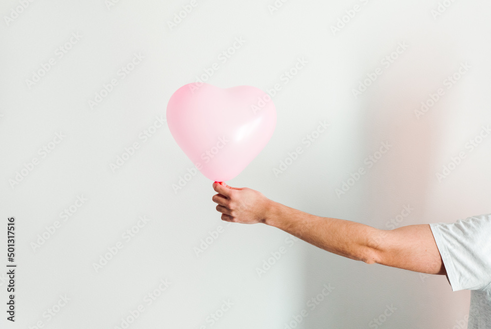 Pink inflatable heart-shaped balloon in hand. White background. Pink inflatable heart-shaped balloon in hand. White background.