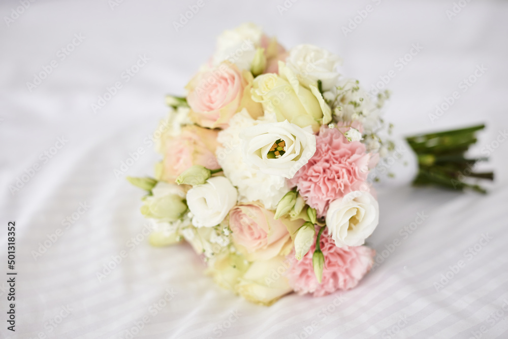 Beautiful flowers bouquet lying on white sheets. Pink, white, ivory roses as a wedding present. Festive decorations for holiday. Symbolism and wedding traditions. Beautiful flowers bouquet lying on white sheets. Pink, white, ivory roses as a wedding present. Festive decorations for holiday. Symbolism and wedding traditions.