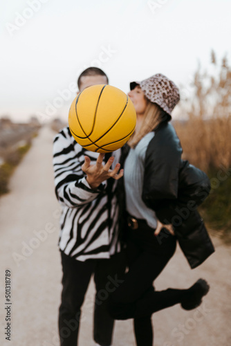 Couple secretly kissing behind a yellow basketball