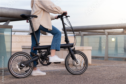 Zero emission concept. Cropped woman legs riding an electric bicycle around the city wearing a casual outfit
