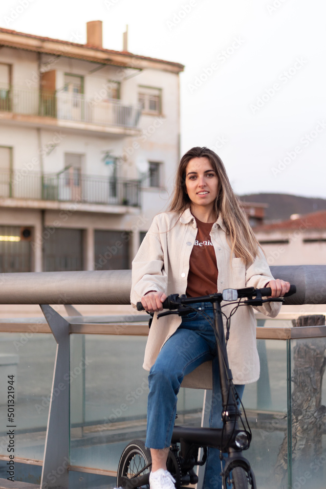Vertical portrait of young woman looking at camera holding an electric bicycle in an urban enviroment Vertical portrait of young woman looking at camera holding an electric bicycle in an urban enviroment