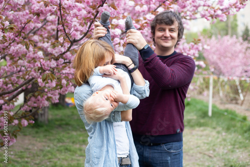 parents and little baby boy son having fun in spring park near pink sakura blooming tree. Spring concept