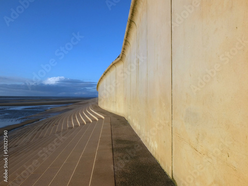 perspective view of the concrete seawall in blackpool with steps leading down to the beach in warm afternoon sunlight with blue cloudy sky