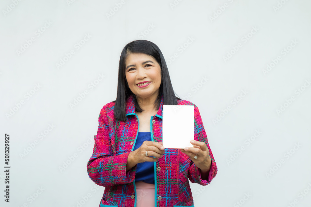Close up cnfident middle-aged Asian woman wearing pink casual wear holding and pointing a white box on her hand on white background. Close up cnfident middle-aged Asian woman wearing pink casual wear holding and pointing a white box on her hand on white background.