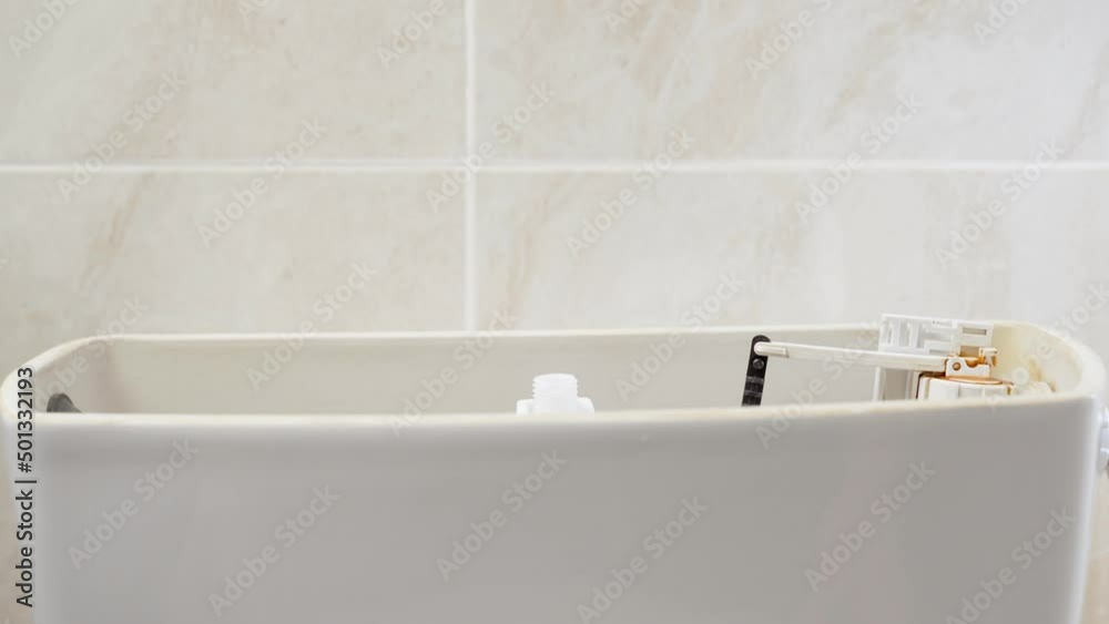 Hands remove the lid of the toilet bowl and unscrew the fittings of the