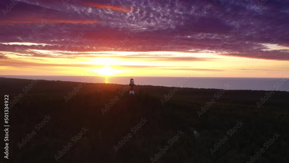 Beautiful sunset over green forest. View of the lighthouse. Orange sun, pastel pink clouds, red sky. Slow drone flight. Beautiful sunset over green forest. View of the lighthouse. Orange sun, pastel pink clouds, red sky. Slow drone flight.