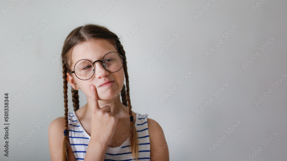 Girl child schoolgirl with pigtails in round glasses shows a finger, copy space and a light beige background Girl child schoolgirl with pigtails in round glasses shows a finger, copy space and a light beige background