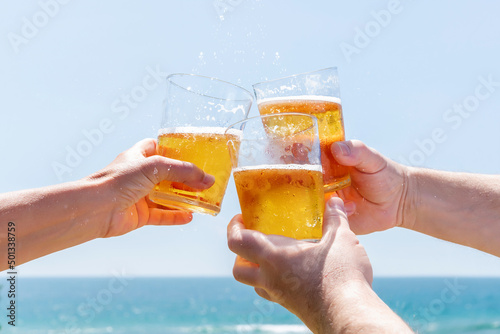 Three friends toasting with beer on a beach in front of the sea. Happy and fun summer