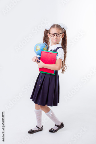 a little girl in glasses and a school uniform holds a book and a globe isolated on a white background © Olesya Pogosskaya