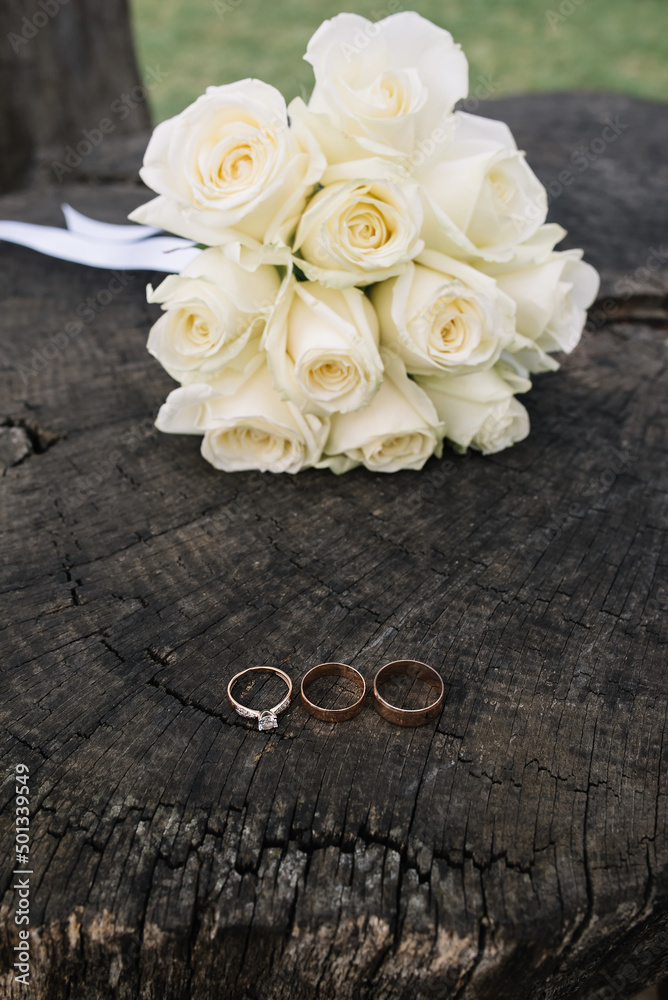 Wedding details. Wedding gold rings with diamond and wedding bouquet of white roses on the wooden background Wedding details. Wedding gold rings with diamond and wedding bouquet of white roses on the wooden background