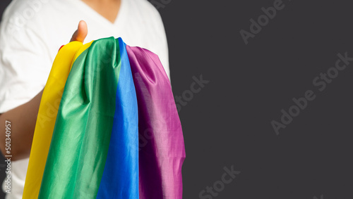 Close-up of hand holding the rainbow flag or LGBT flag while standing on a gray background