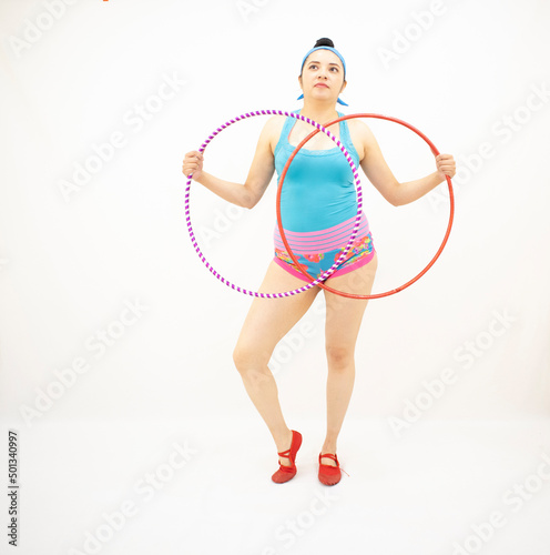 young white woman holding two hula hoops, blue blouse, short pink, with white background