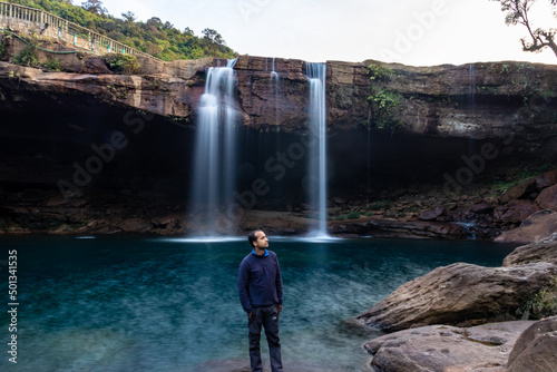 young man with waterfall streams falling from mountain top at morning long exposure shot