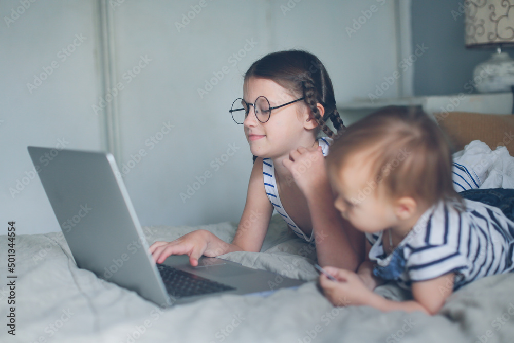Girl child and Baby Toddler with laptop and bank card, together make an order on Internet, online shopping and children, toddler and older sister with laptop on bed in bedroom Girl child and Baby Toddler with laptop and bank card, together make an order on Internet, online shopping and children, toddler and older sister with laptop on bed in bedroom