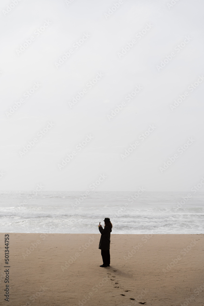 someone walking alone on the beach on a foggy day with a mobile phone